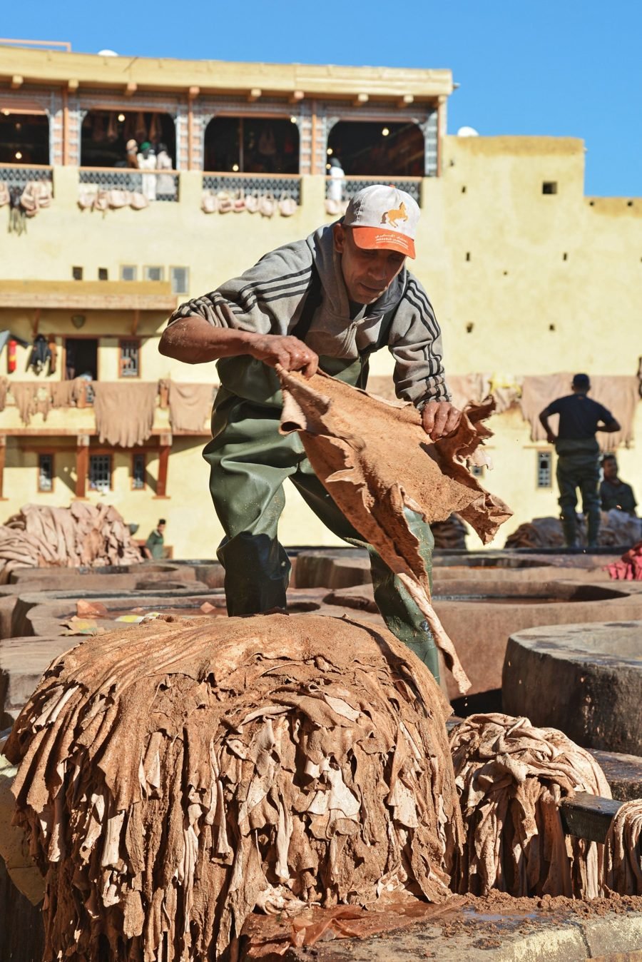 Artisan tanneur retournant des peaux au-dessus des cuves d'une tannerie traditionnelle marocaine